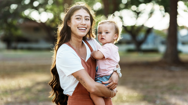 Young smiling mother holder a toddler in her arms in a park